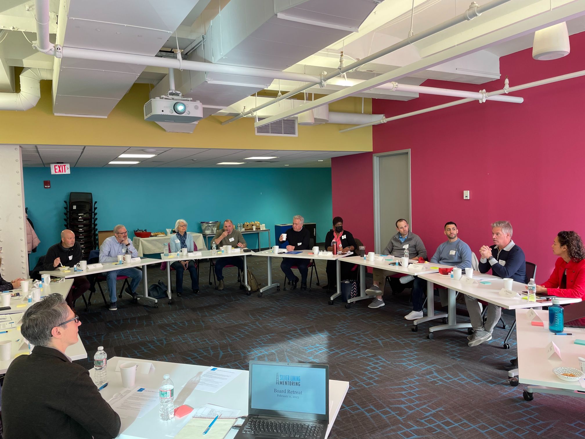 SLM board members sit at tables around a room with pink and blue walls.